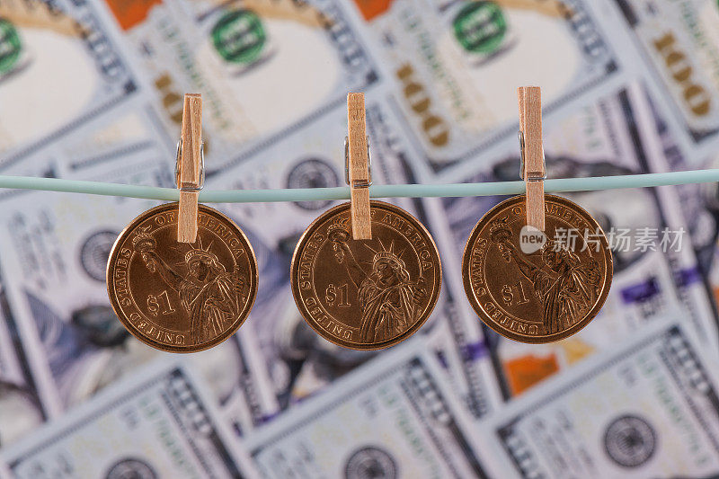 三枚1美元面值的硬币挂在一根绳子上，背景是100美元纸币