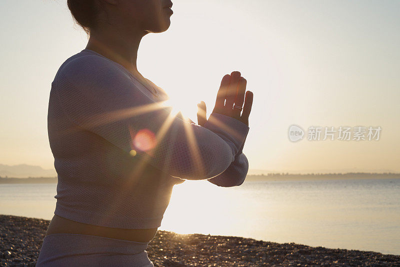 健康的年轻女子坐在瑜伽莲花姿势与闭上眼睛在大海前，在海滩上的日出冥想。