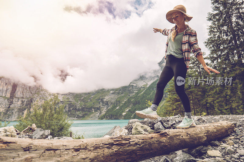 年轻女子走在树干附近高山湖泊找到平衡手臂在她的身边，自然人达到成功的概念