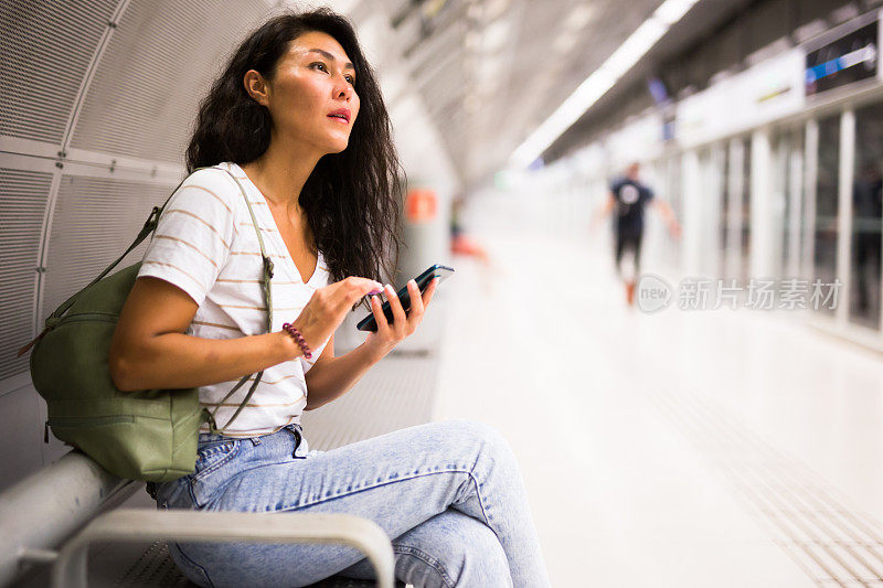 女人拿着智能手机坐在地铁站的长椅上