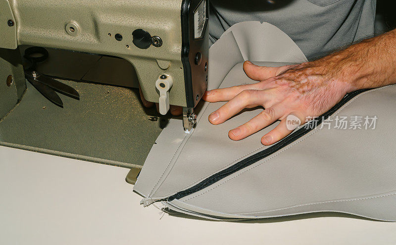 一名男子正在缝纫机上给裁剪好的衣服缝线。软垫家具的修理和装饰