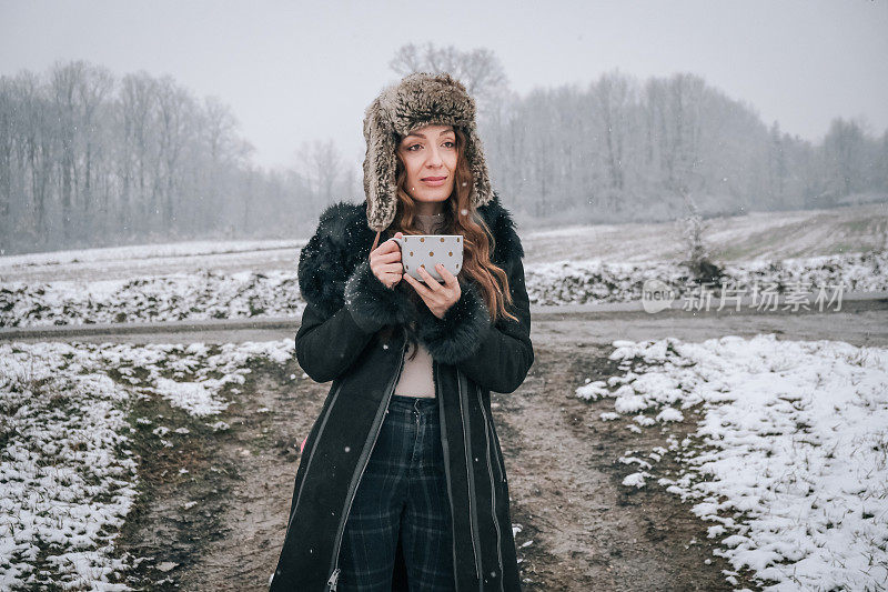 站在雪地上拿着一杯茶的年轻女子