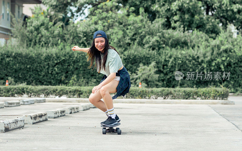 肖像美丽的运动亚洲女滑冰运动员穿着潮衬衫与短裤，微笑与幸福，站在滑板和户外玩与复制空间。活动和冒险概念。