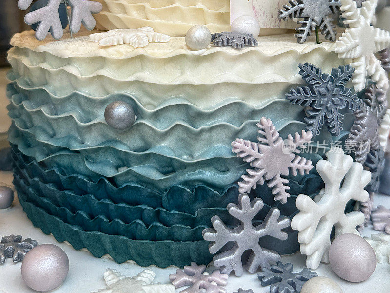 冬季主题的分层生日蛋糕的特写图像装饰在蛋糕板上的彩色黄油糖衣，珠光翻糖糖衣形状像球和雪花，重点在前景