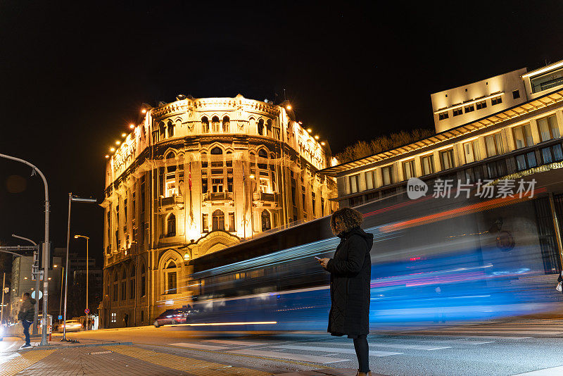 黄昏时分，城市灯光和街道上流动的交通。人行道上的女人在用手机