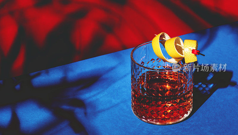 萨泽拉克，经典的酒精鸡尾酒，加入干邑，波旁，苦艾酒，苦味酒，糖和柠檬皮。耀眼的红蓝色背景与硬光和粗糙的阴影