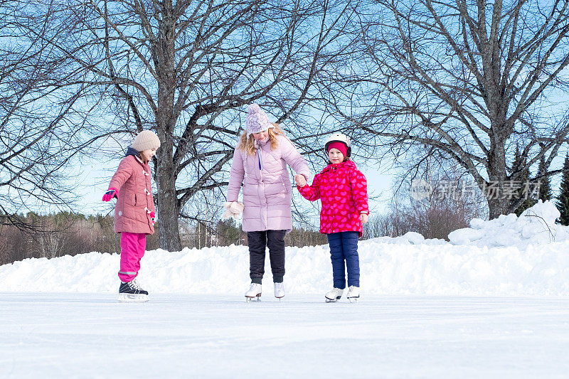 两个白人女孩，7岁，正在训练滑冰。一位妇女训练孩子们正确地站在冰鞋上。
