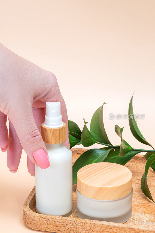 女人的手摸着一个白色乳霜的瓶子模型。未标示的化妆品包装在阳光下的米色背景。护肤概念