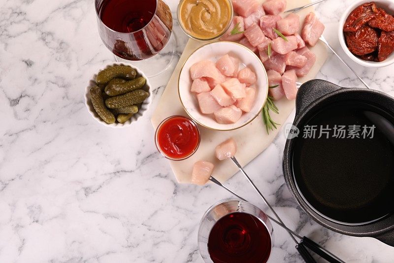 火锅锅用油、叉子、生肉块、红酒杯等产品放在白色大理石桌上，平铺。文本空间