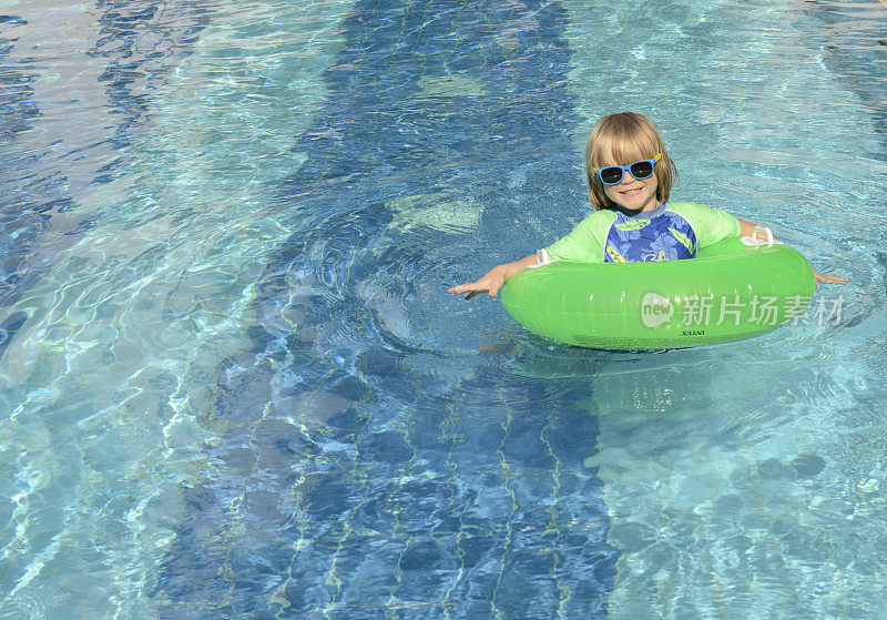 积极的男孩，有一个充气圈和一个床垫在游泳池附近。在度假胜地度假的孩子。家庭旅馆