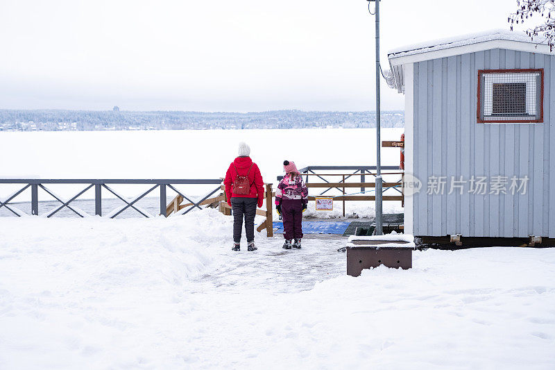 一个年轻女子和一个8岁的小女孩，在一个白雪覆盖的湖边。冬天人们在冰洞里游泳的地方。
