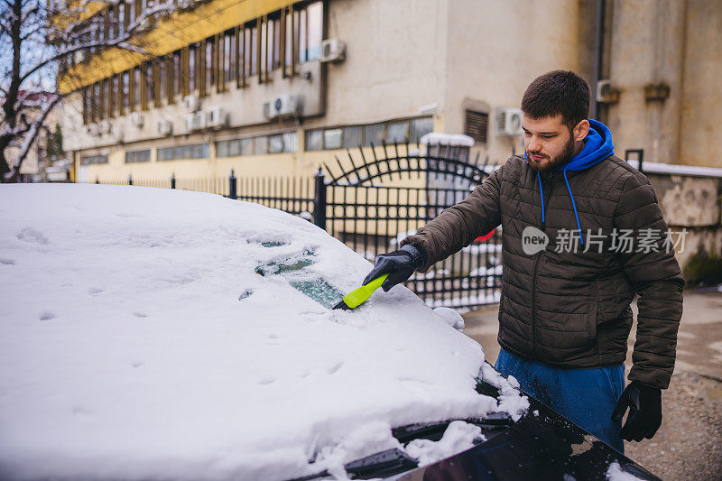 年轻人正在清除汽车上的积雪