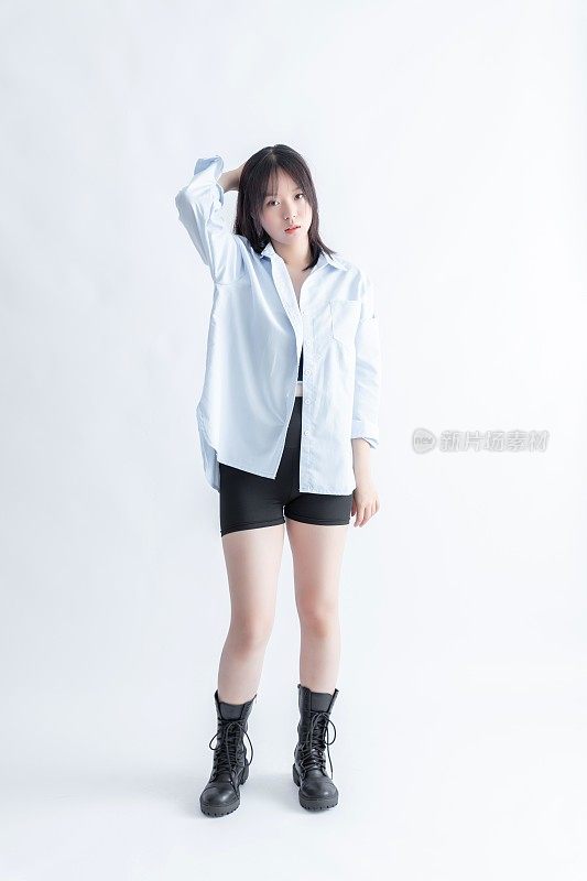 一个年轻的亚洲女人穿着浅蓝色的超大号衬衫和黑色短裤，在白色的背景下摆姿势