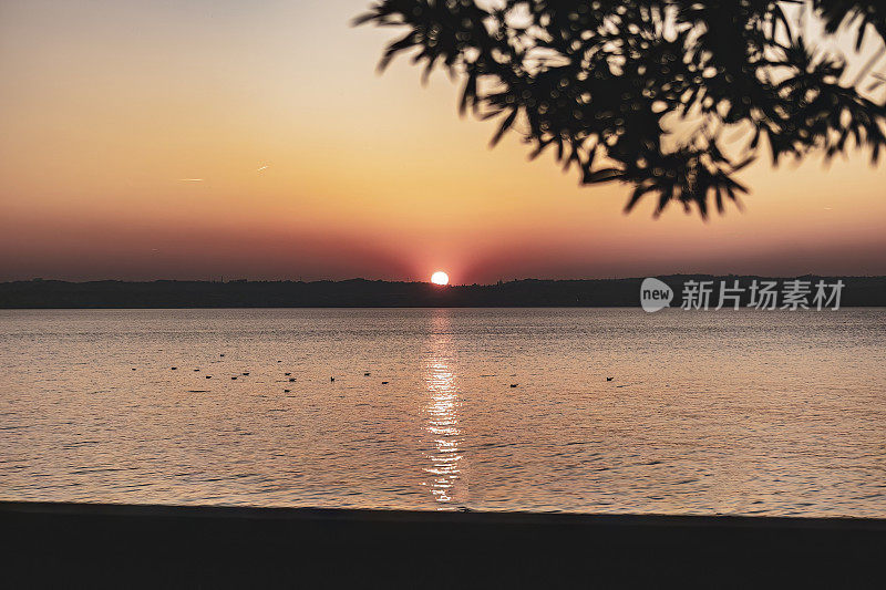 意大利加尔达湖上美丽的日落，太阳反射在平静的水面上