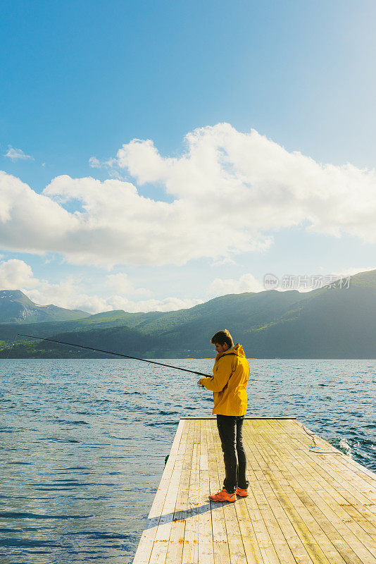 夏天在挪威峡湾与山景钓鱼的黄夹克男子