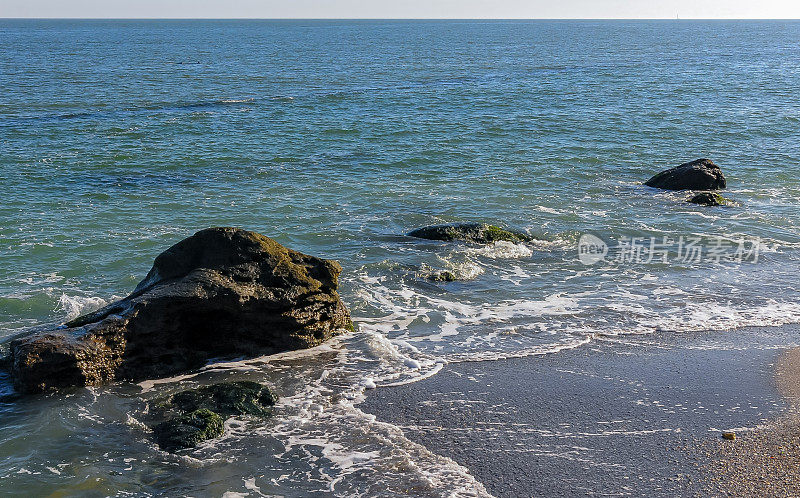 在阳光明媚的日子里，明亮的倒影在水面上的海岸岩石附近，海浪与白色泡沫翻滚在沙滩上，太阳在水面上的反射，黑海海岸