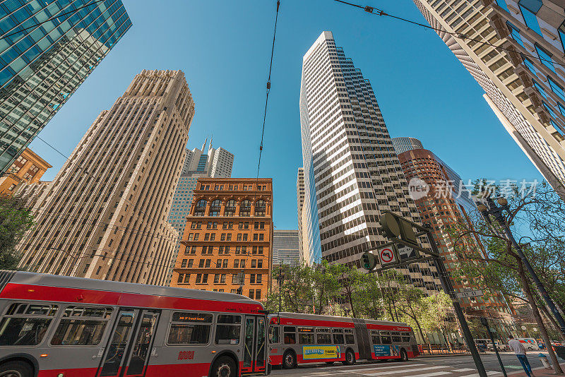 在旧金山，红色巴士从高耸的现代和古典建筑下穿行。