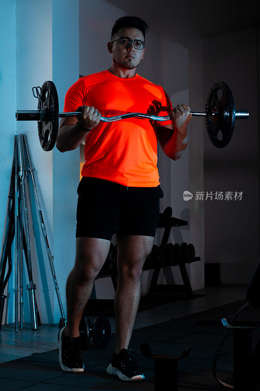生活方式:穿着橙色衬衫的年轻人举重，锻炼肱二头肌