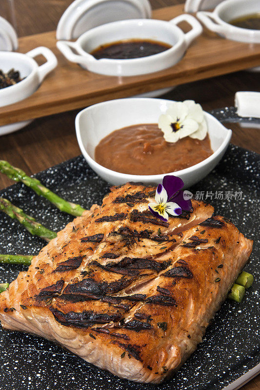 餐厅餐桌上的烤三文鱼配以芦笋、酱汁和调味料，并以鲜花装饰