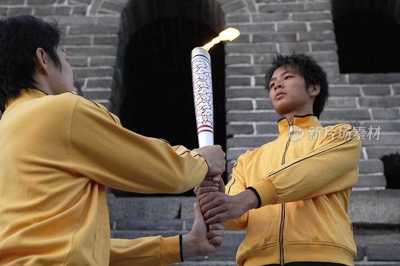 两位身穿运动服的年轻人站在长城烽火台前，举着一支火炬