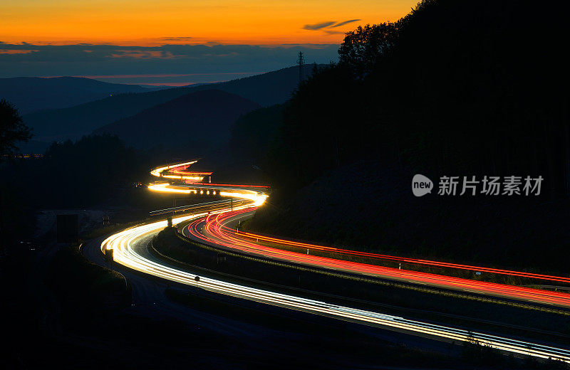 夕阳下，高速公路上蜿蜒的山峦上的车灯长时间曝光