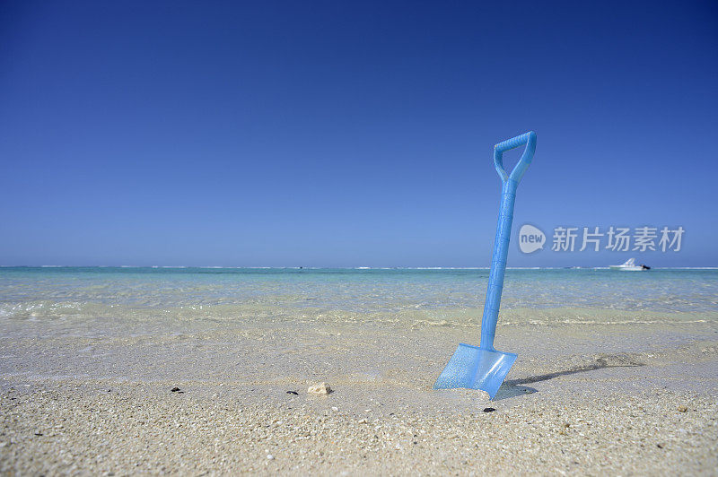 蓝色的玩具铁铲站在毛里求斯海滩的沙滩上