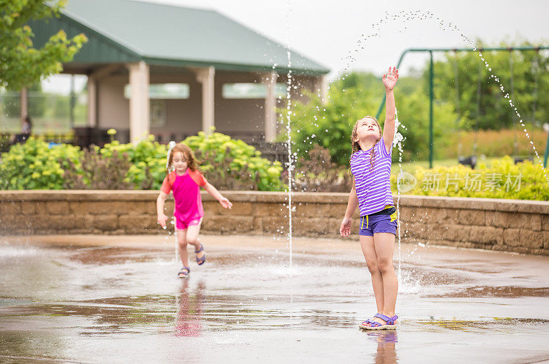 两个女孩在喷泉里玩在夏天的水花公园