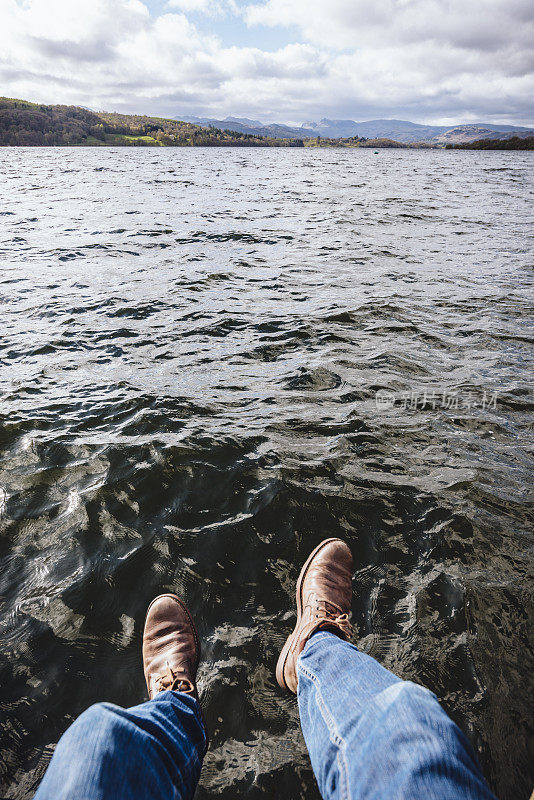 穿着靴子的男人的脚悬挂在温德米尔湖上。