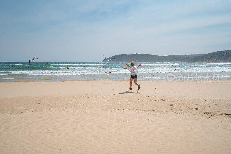 年轻女子在海滩上追逐鸟儿