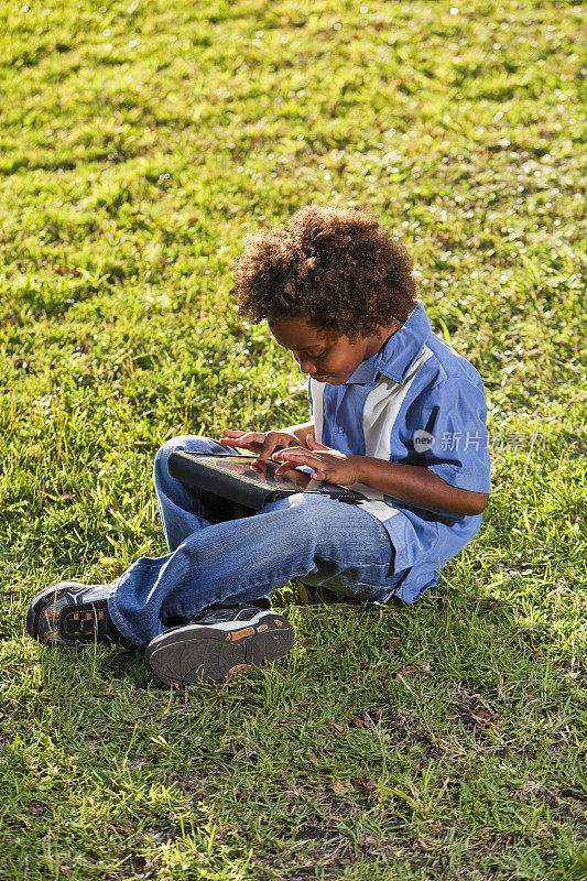 男孩坐在草地上拿着平板电脑