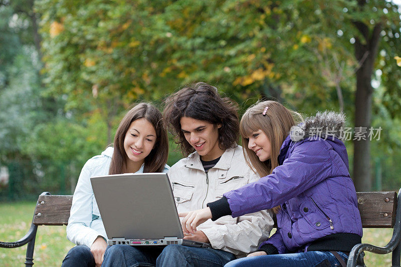 三个拿着笔记本电脑的青少年在公园里。