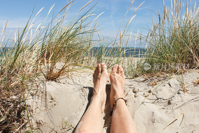 阳光明媚的海滩，女人的脚在沙滩上