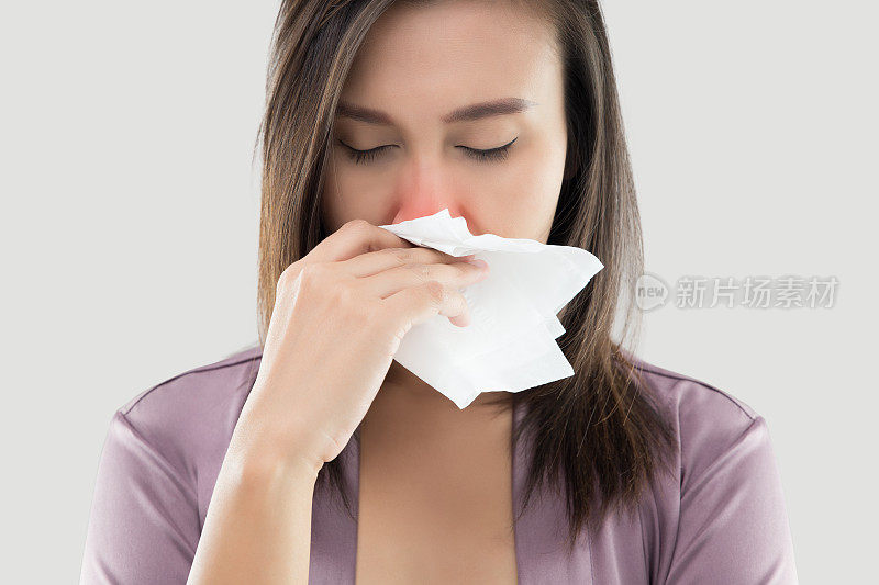 亚洲妇女在缎子睡衣感觉不舒服和打喷嚏对白色的背景，灰尘过敏，流感，人们感冒和过敏