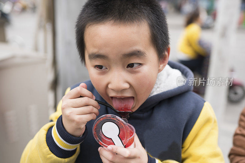 亚洲小学男孩吃果酱在街上高兴