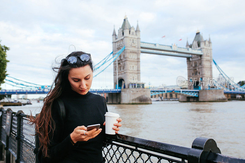 在英国伦敦，年轻的女游客一边喝咖啡，一边用手机发短信