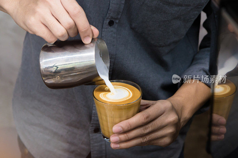 男性咖啡师手握和倒热牛奶准备拿铁咖啡杯上的拿铁艺术的特写