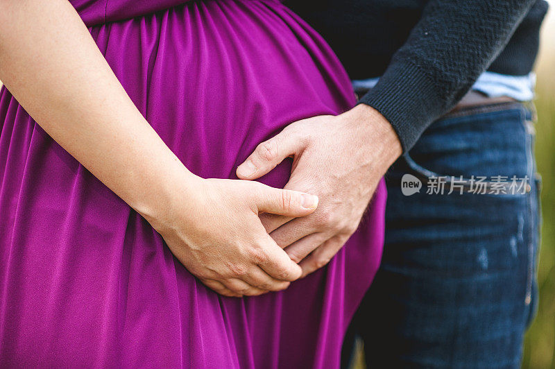 一对夫妇的手放在妇女怀孕的肚子上