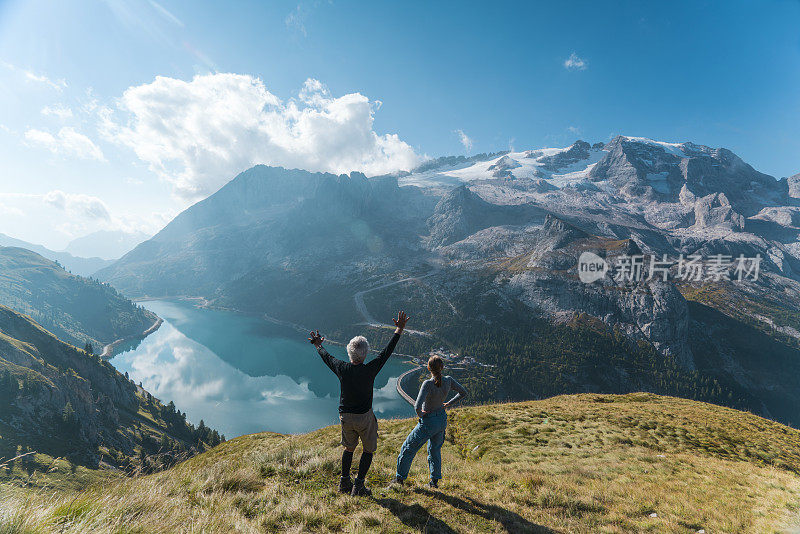 在意大利北部Dolomites的Fedaia山口到Pordoi的小路上休息的地方，一对老人正在欣赏美丽的Fedaia湖和马尔莫拉达山的景色。