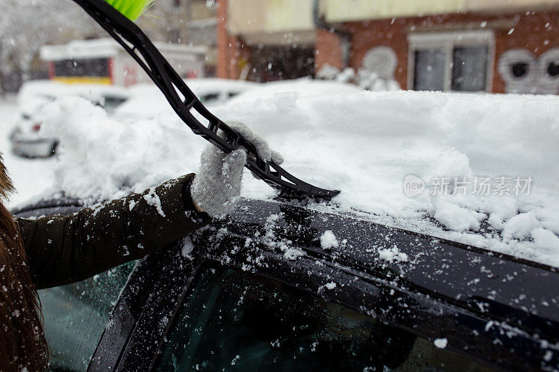 年轻女子在清理车上的积雪