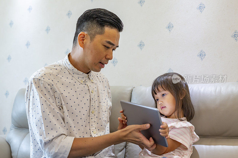 父亲和蹒跚学步的女儿在平板电脑上阅读