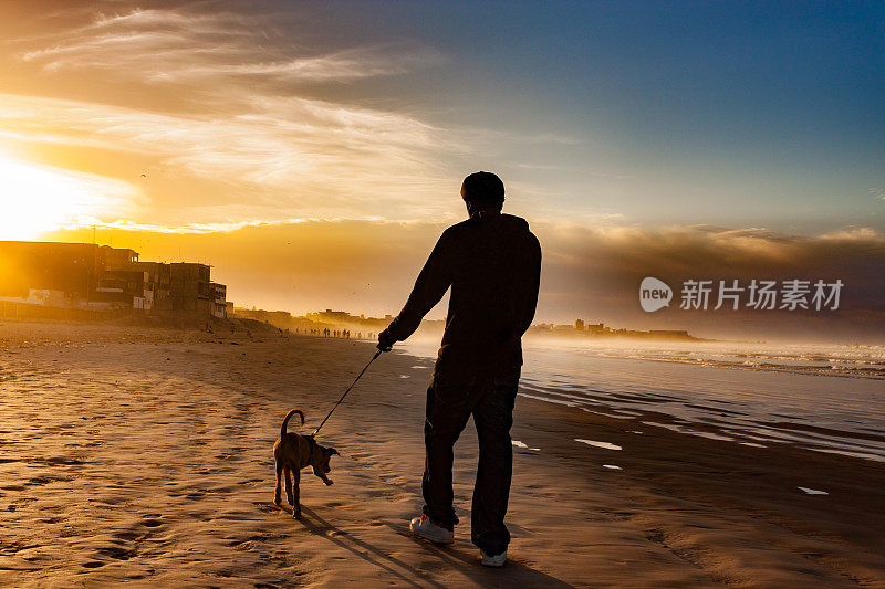 一个年轻人和他的狗在海滩上散步