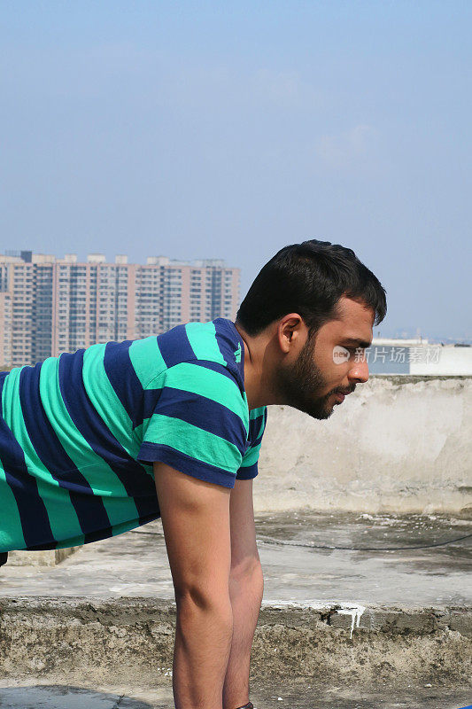 印度男子在屋顶上练习牛(bitilasana)瑜伽姿势，德里，印度