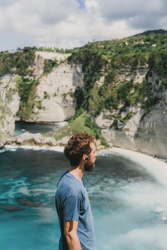 一个戴着无线耳机的男人从努萨佩尼达的悬崖上看海滩的风景
