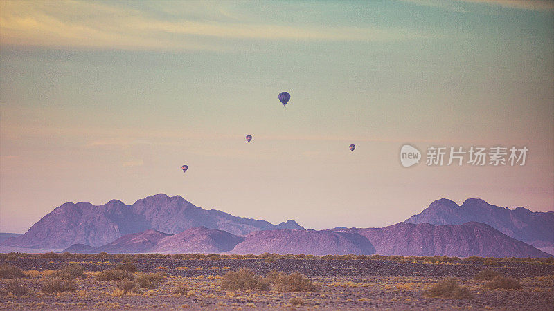一群热气球在粉红色的沙漠景观上飞行