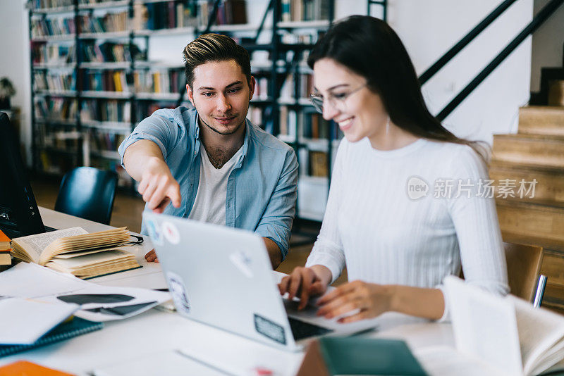 积极的男性指着笔记本电脑显示器，帮助女性安装新的校园教育应用程序，学生们谈论共同的项目，利用wifi在图书馆做网上研究