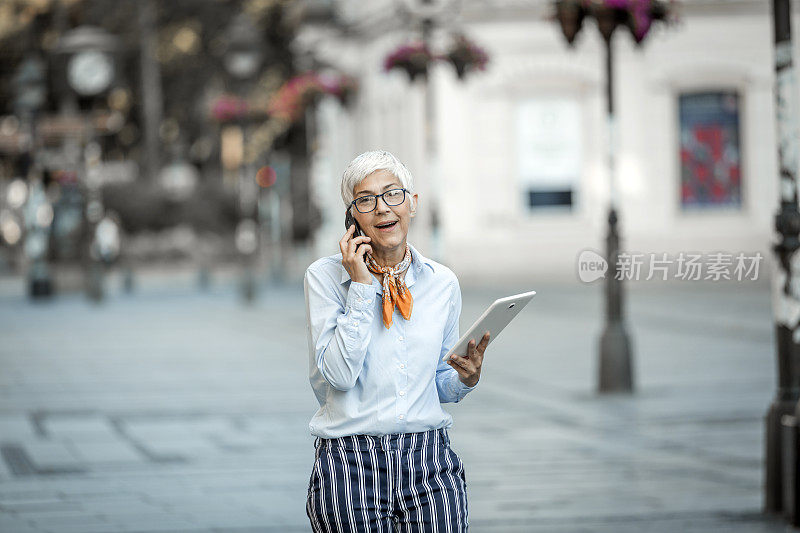 高级女商人正带着她的数字平板电脑走在城市的街道上