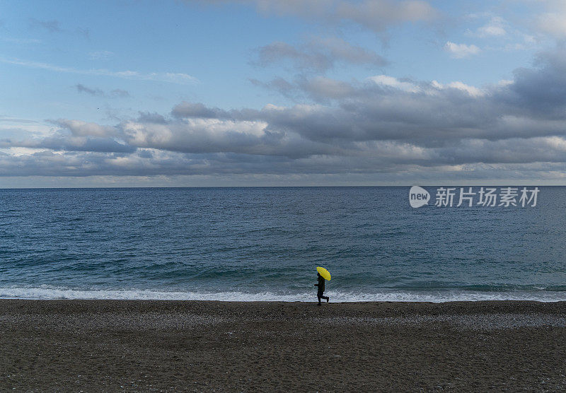 一个孤独的人在雨天走在海滩上