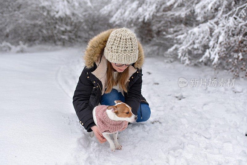 年轻的女人和狗在白雪覆盖的森林