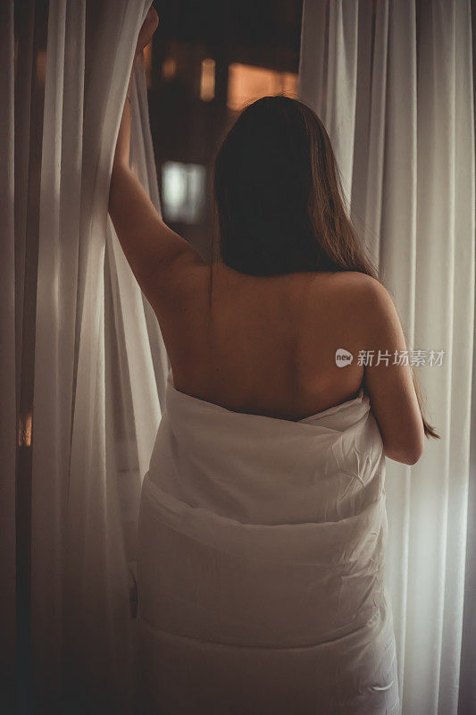 一个裹着亚麻布的女人站在窗边