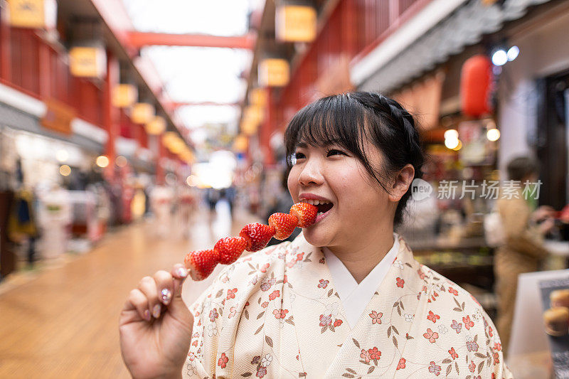 穿着和服的日本妇女在购物街上吃草莓